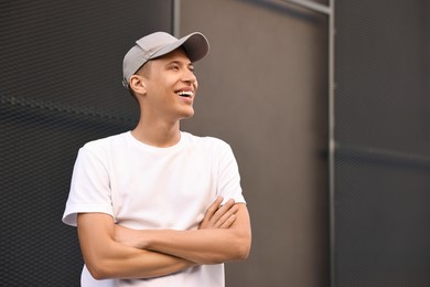 Smiling man in baseball cap near dark wall. Space for text