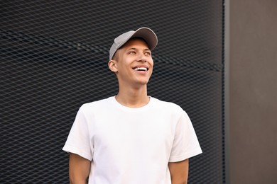 Portrait of smiling man in baseball cap near dark wall