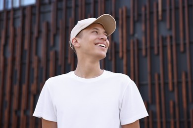 Portrait of smiling man in baseball cap near dark wall, low angle view