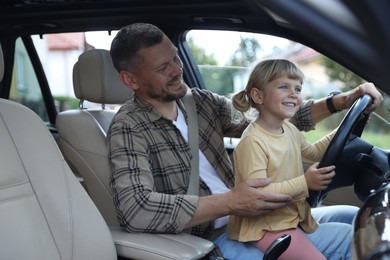 Photo of Happy man with his daughter holding steering wheel inside car