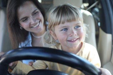 Photo of Happy woman with her daughter holding steering wheel inside car, selective focus