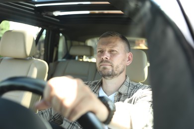 Man holding steering wheel while driving car, view through windshield