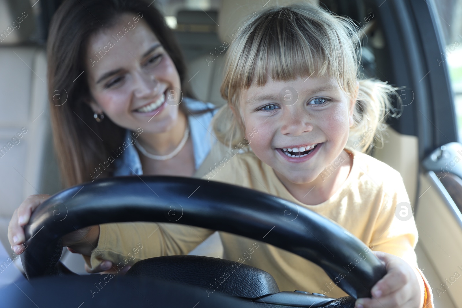 Photo of Happy woman with her daughter holding steering wheel inside car, selective focus