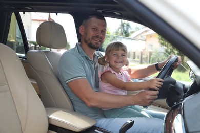 Photo of Happy man with his daughter holding steering wheel inside car