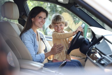 Happy woman with her daughter holding steering wheel inside car