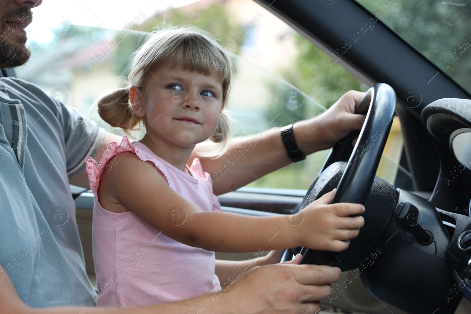 Photo of Man with his daughter holding steering wheel inside car, closeup