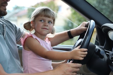 Man with his daughter holding steering wheel inside car, closeup