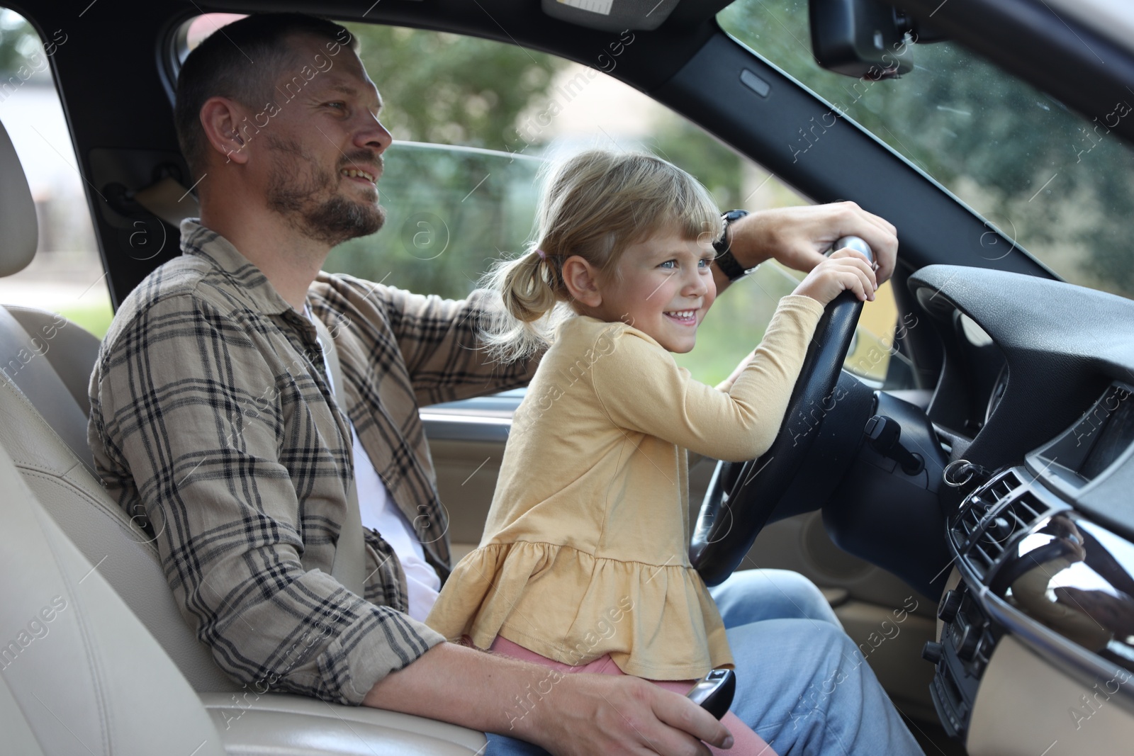 Photo of Happy man with his daughter holding steering wheel inside car