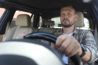 Man holding steering wheel while driving car, view through windshield