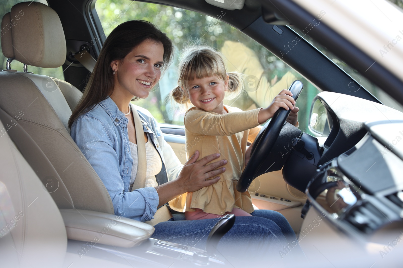 Photo of Happy woman with her daughter holding steering wheel inside car