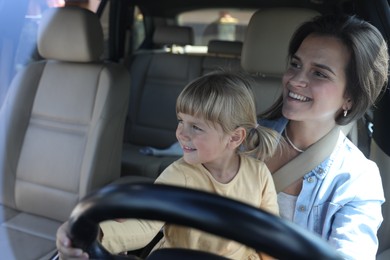 Happy woman with her daughter holding steering wheel inside car, view through windshield