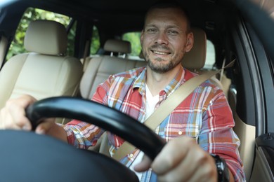 Photo of Smiling man holding steering wheel while driving car, view through windshield