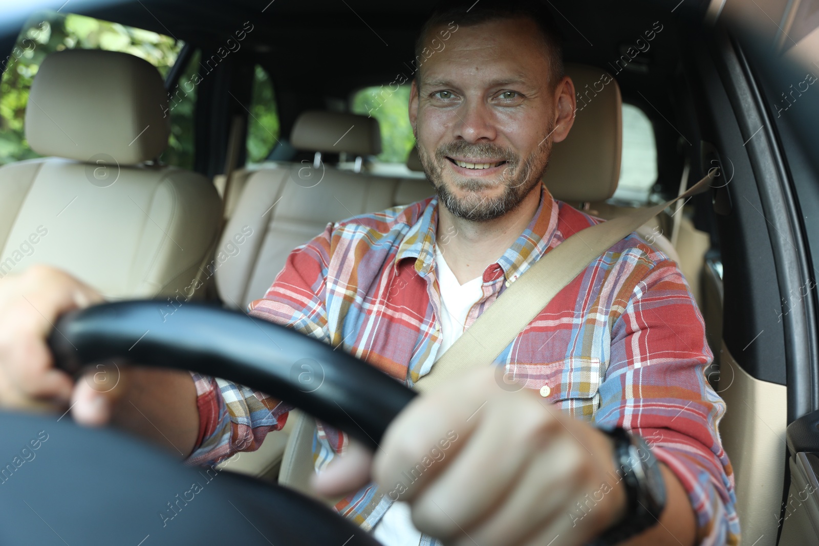 Photo of Smiling man holding steering wheel while driving car, view through windshield