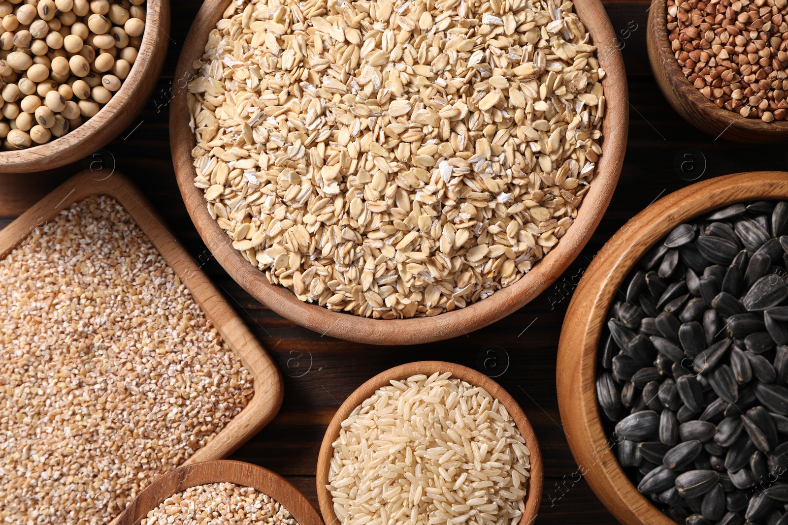 Photo of Different types of cereals, seeds and legumes in bowls on wooden table, flat lay