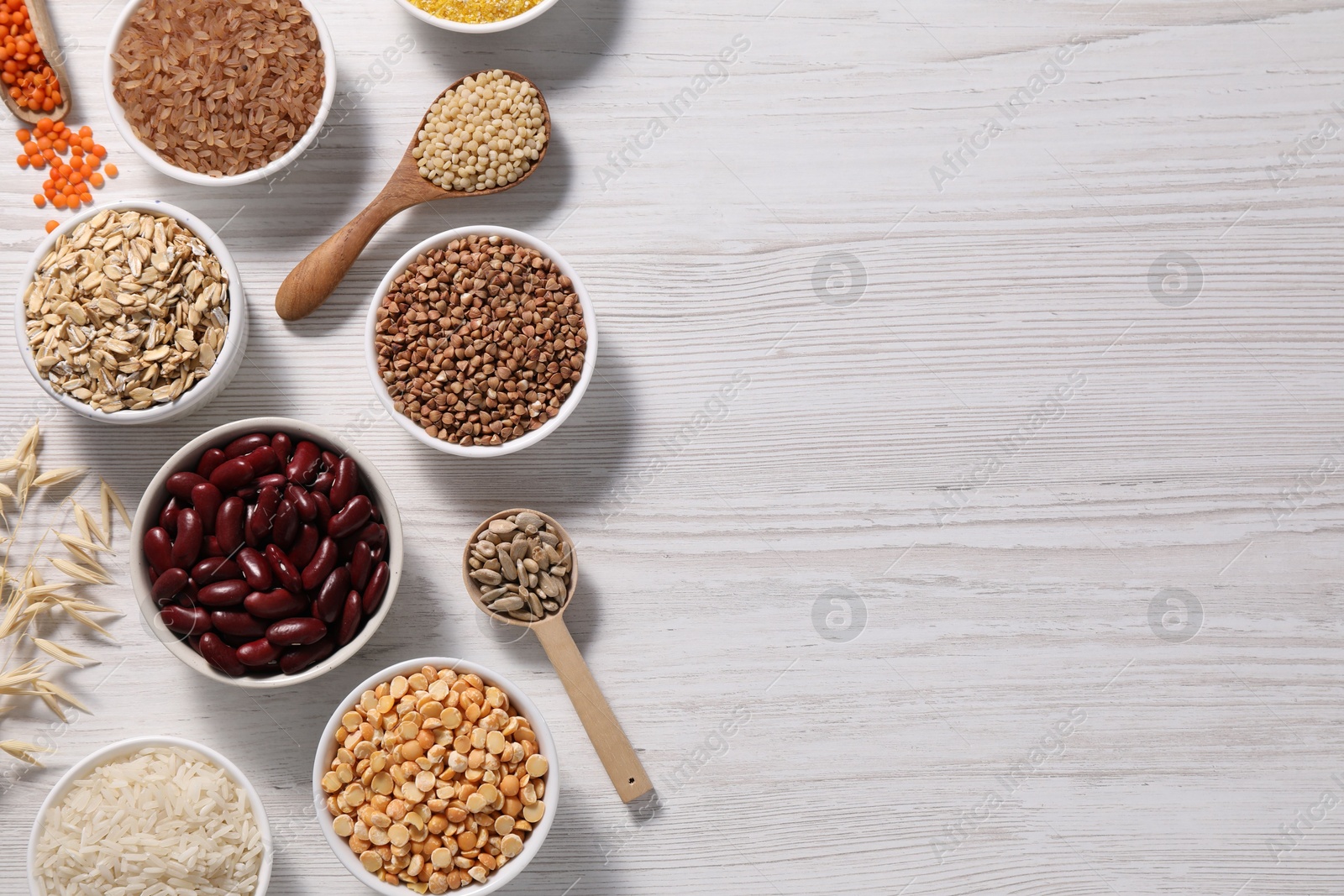 Photo of Different types of cereals, seeds and legumes on white wooden table, flat lay. Space for text