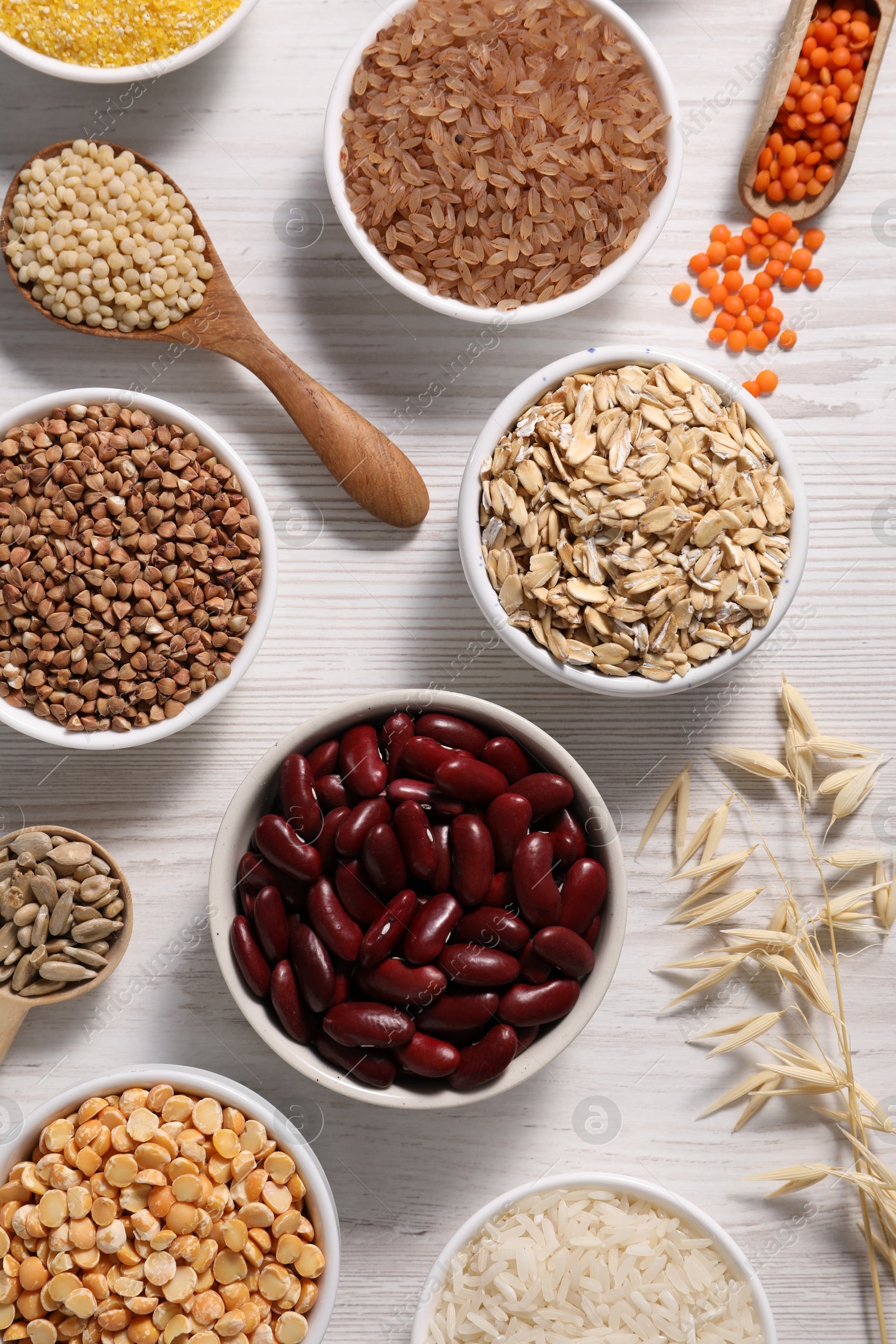 Photo of Different types of cereals, seeds and legumes on white wooden table, flat lay