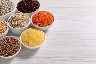 Photo of Different types of cereals and legumes in bowls on white wooden table. Space for text