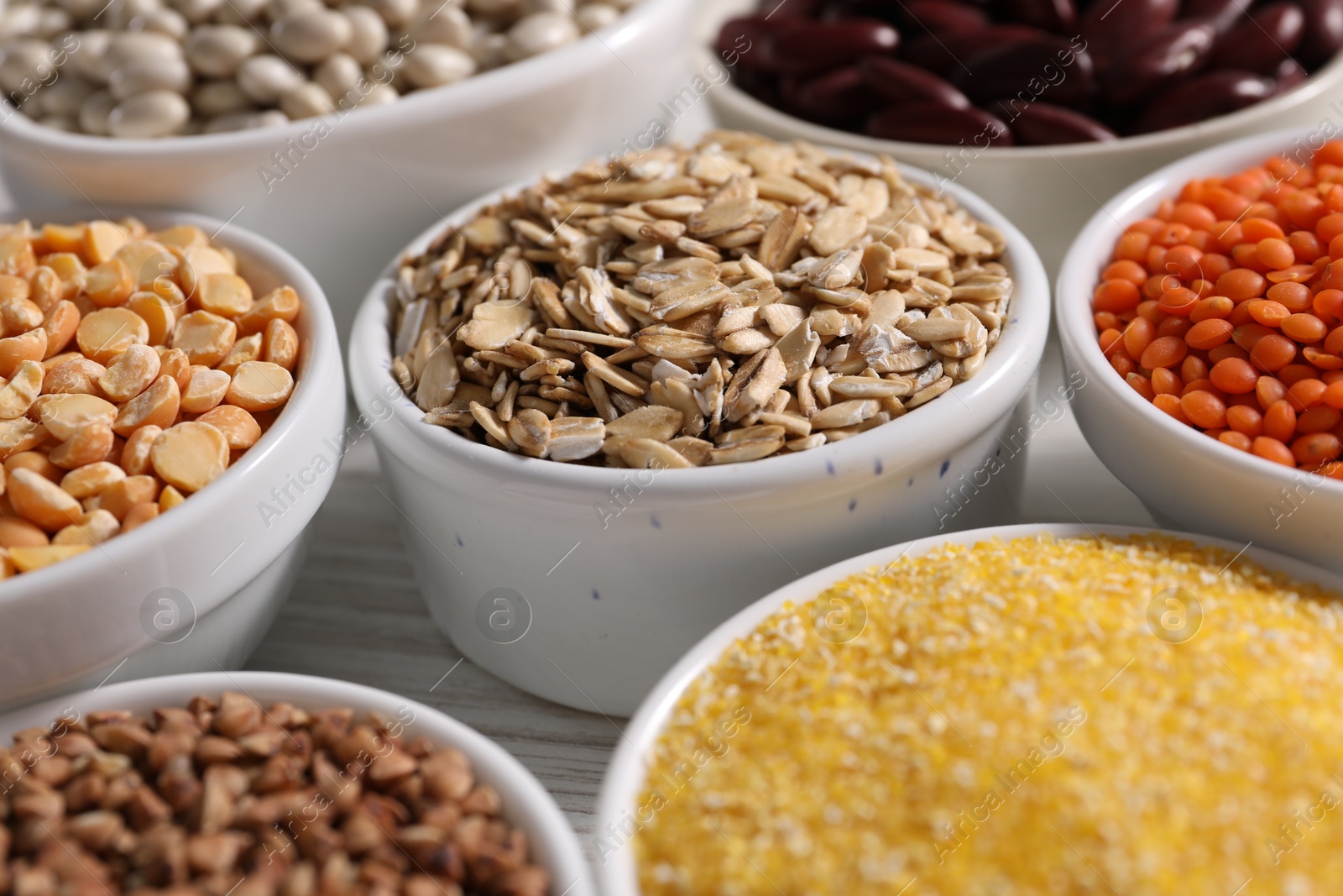 Photo of Different types of cereals and legumes in bowls on white table, closeup