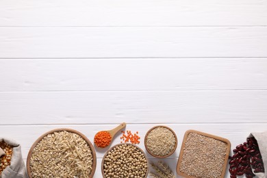 Photo of Different types of cereals and legumes on white wooden table, flat lay. Space for text