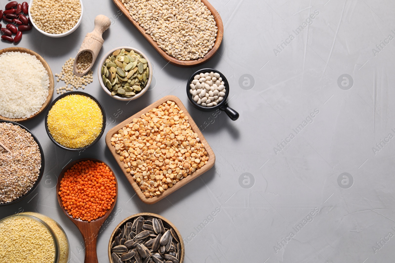 Photo of Different types of cereals, seeds and legumes on grey table, flat lay. Space for text