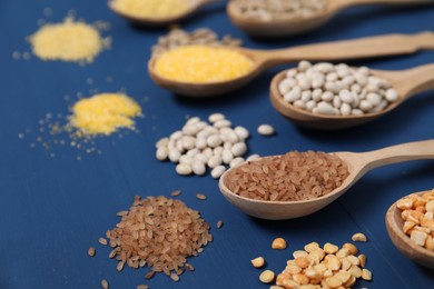 Photo of Different types of cereals and legumes in spoons on blue wooden table, closeup