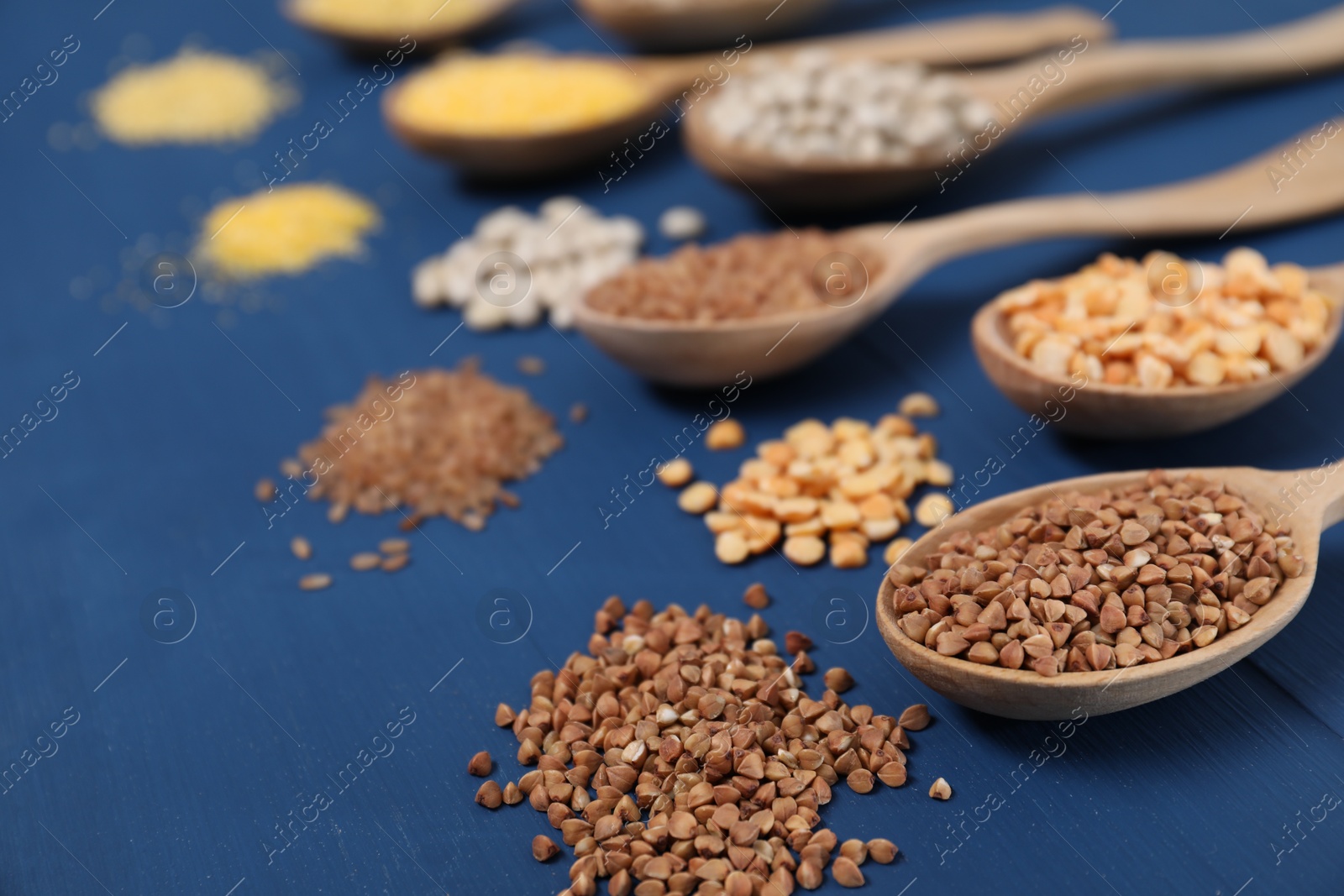 Photo of Different types of cereals and legumes in spoons on blue wooden table, closeup