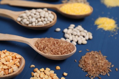 Photo of Different types of cereals and legumes in spoons on blue wooden table, closeup