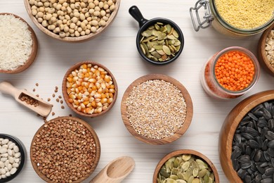 Photo of Different types of cereals, seeds and legumes on white wooden table, flat lay