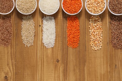 Photo of Different types of cereals and legumes in bowls on wooden table, flat lay. Space for text