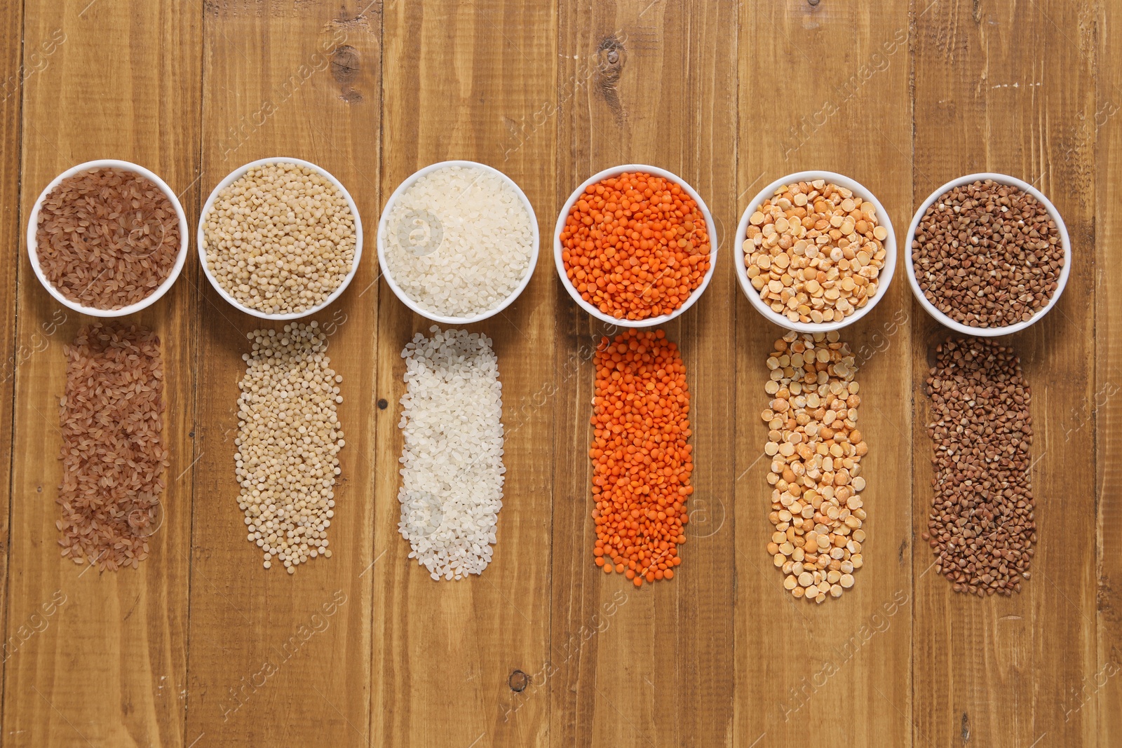 Photo of Different types of cereals and legumes in bowls on wooden table, flat lay