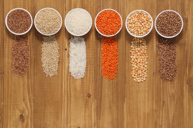 Photo of Different types of cereals and legumes in bowls on wooden table, flat lay. Space for text