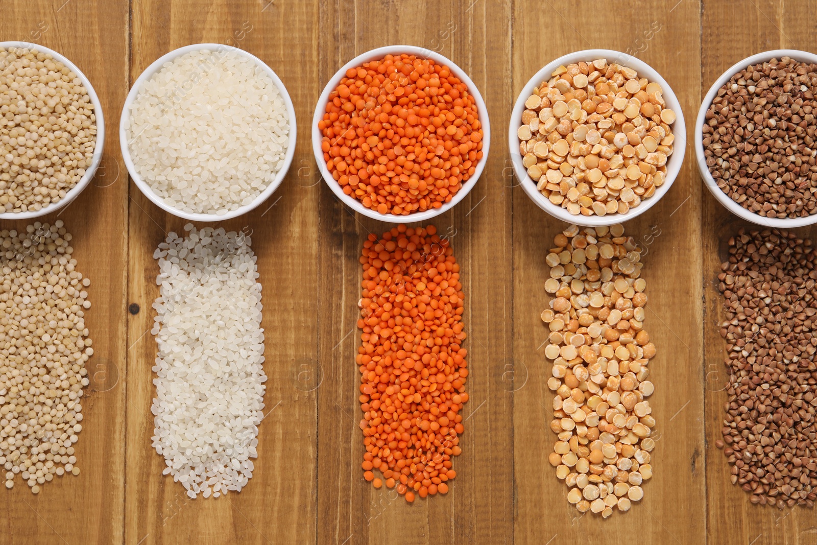 Photo of Different types of cereals and legumes in bowls on wooden table, flat lay