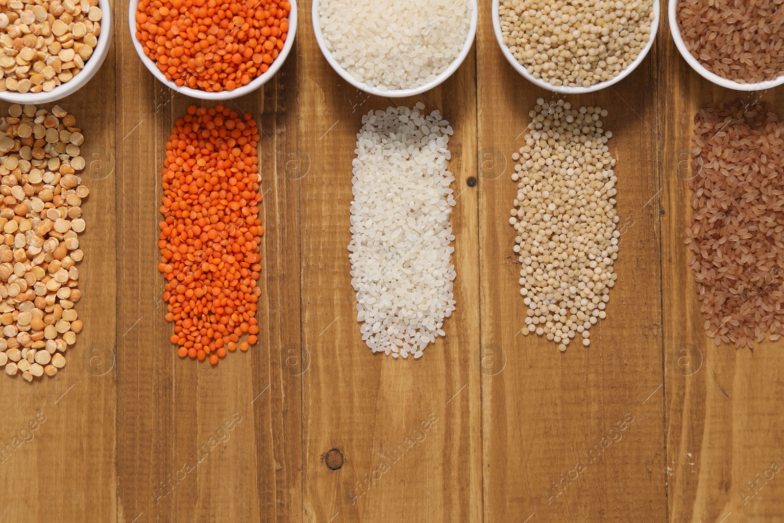 Photo of Different types of cereals and legumes in bowls on wooden table, flat lay. Space for text