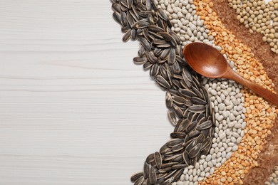 Photo of Different types of cereals, seeds and legumes with spoon on white wooden table, flat lay. Space for text