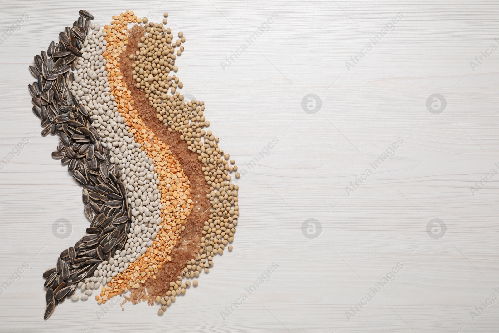 Photo of Different types of cereals, seeds and legumes on white wooden table, flat lay. Space for text