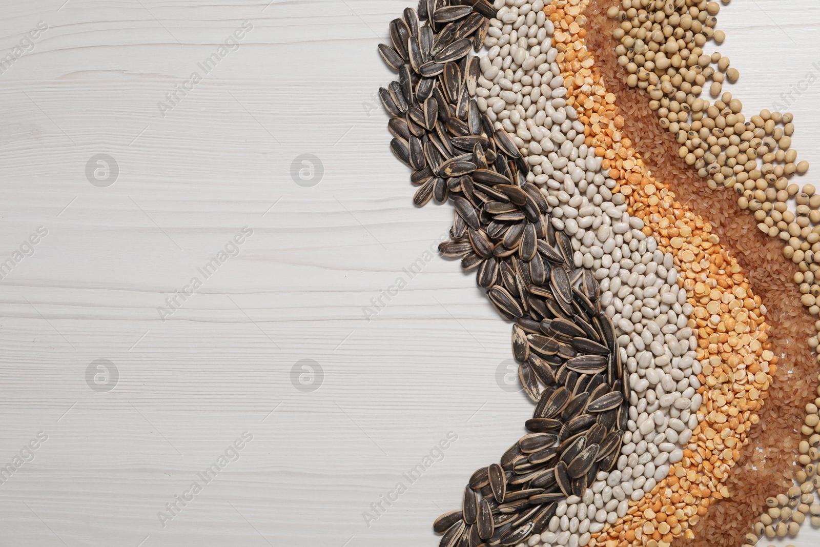 Photo of Different types of cereals, seeds and legumes on white wooden table, flat lay. Space for text