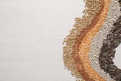 Photo of Different types of cereals, seeds and legumes on white wooden table, flat lay. Space for text