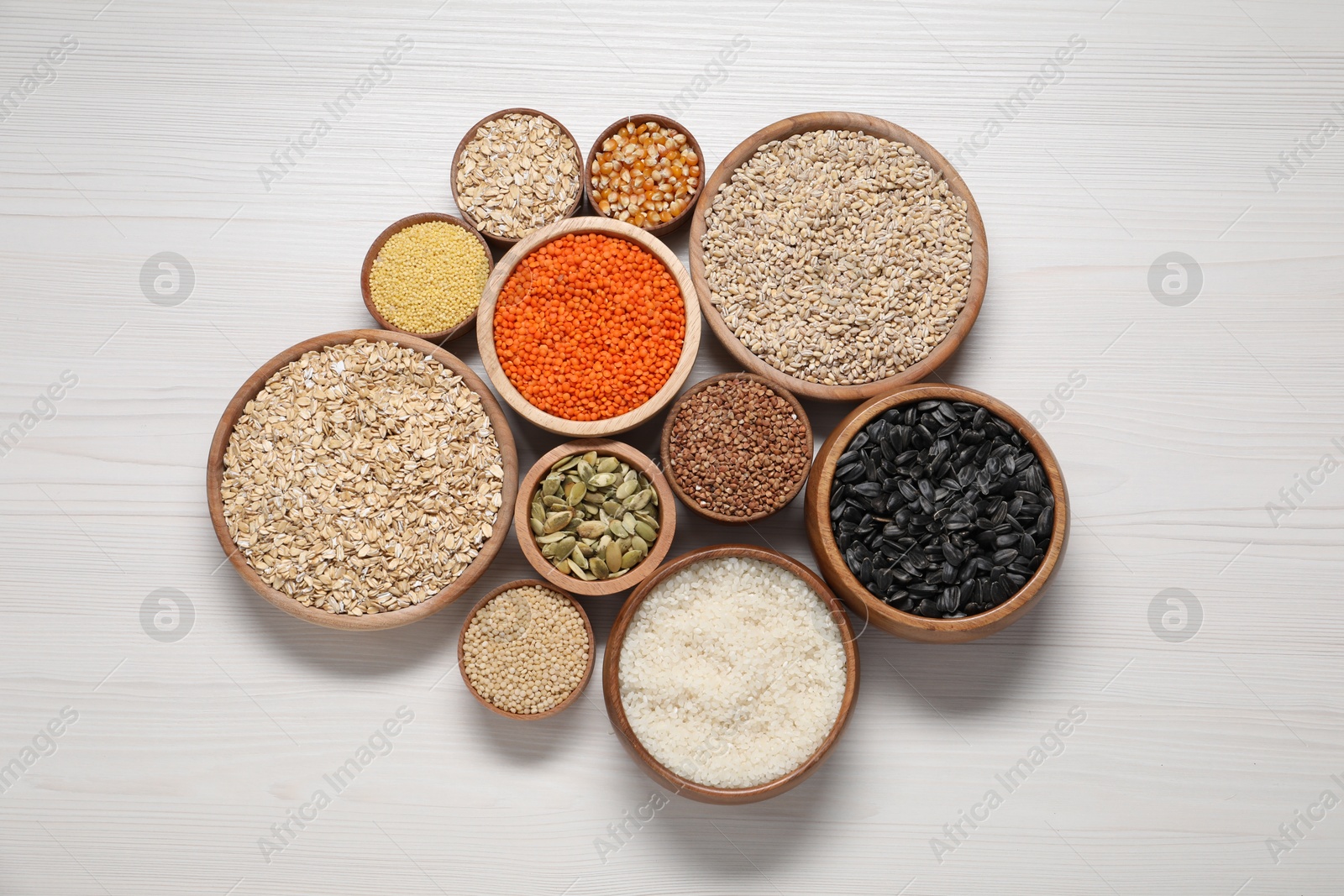 Photo of Different types of cereals, seeds and legumes in bowls on white wooden table, flat lay