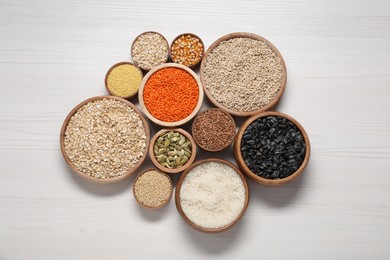 Photo of Different types of cereals, seeds and legumes in bowls on white wooden table, flat lay