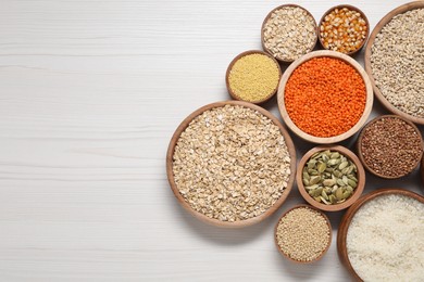 Photo of Different types of cereals, seeds and legumes in bowls on white wooden table, flat lay. Space for text