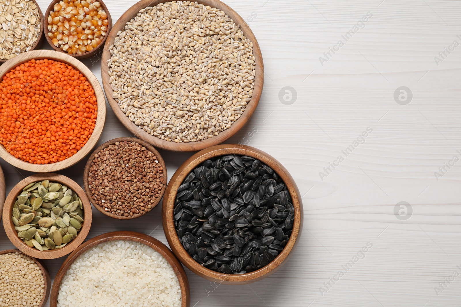 Photo of Different types of cereals, seeds and legumes in bowls on white wooden table, flat lay. Space for text