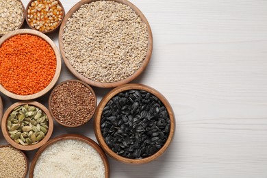 Different types of cereals, seeds and legumes in bowls on white wooden table, flat lay. Space for text