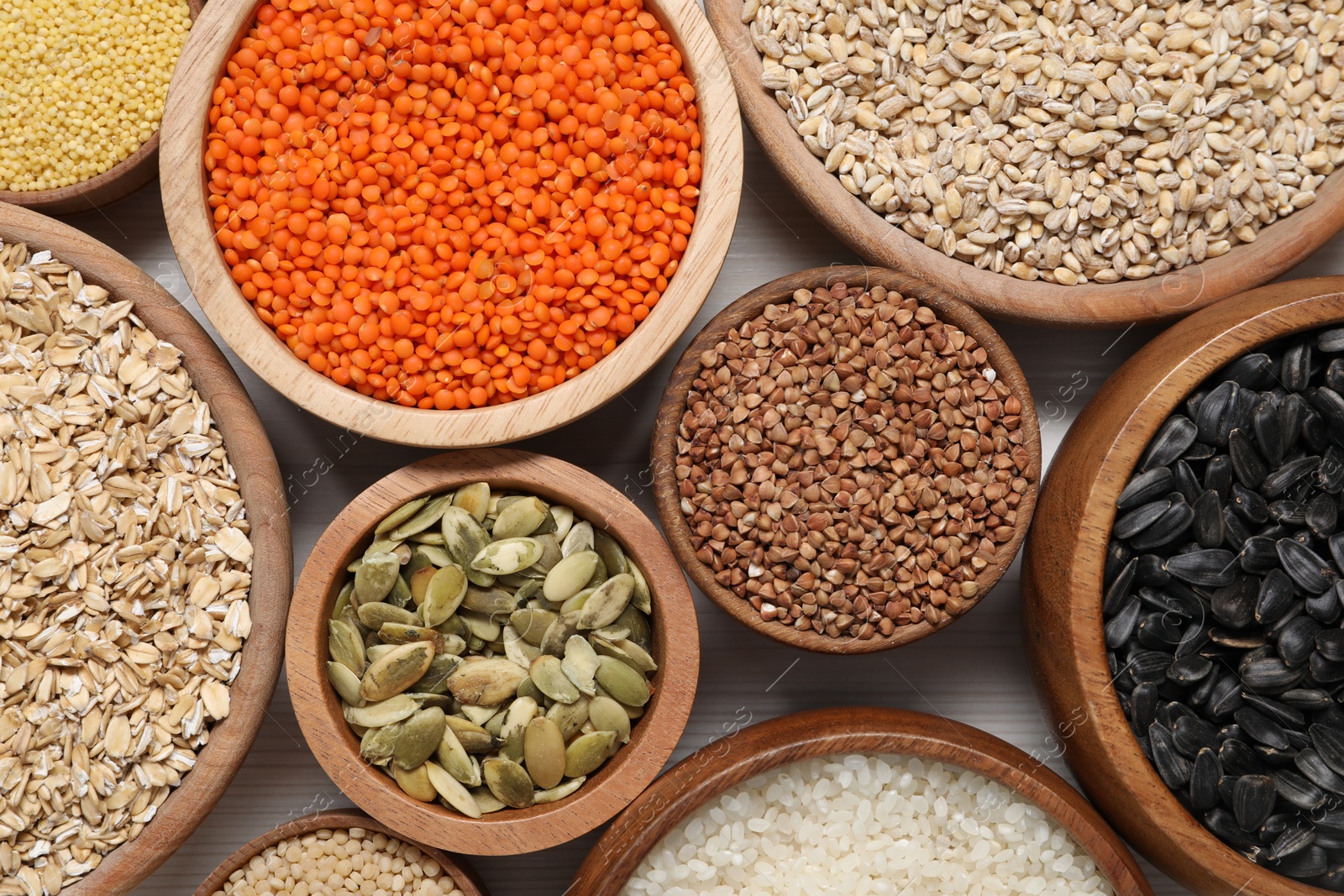 Photo of Different types of cereals, seeds and legumes in bowls on white table, flat lay