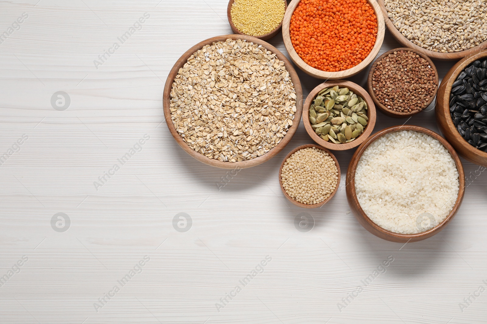 Photo of Different types of cereals, seeds and legumes in bowls on white wooden table, flat lay. Space for text