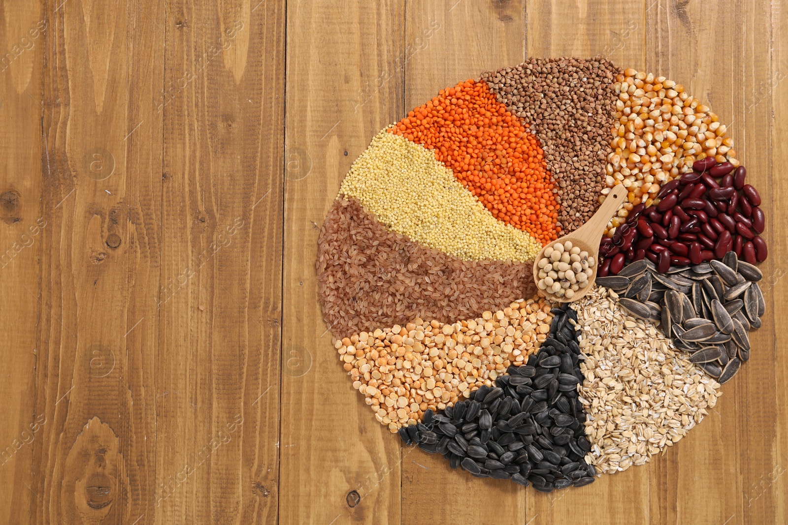 Photo of Different types of cereals, legumes and seeds with spoon on wooden table, top view. Space for text