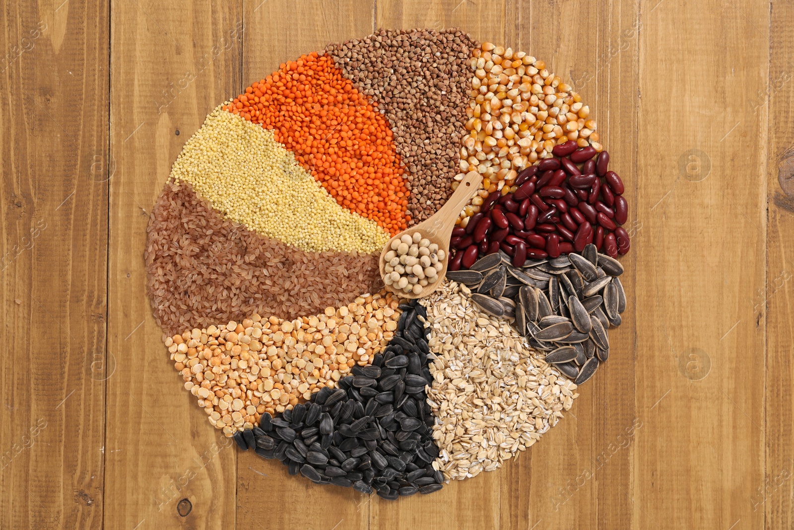 Photo of Different types of cereals, legumes and seeds with spoon on wooden table, top view