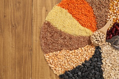 Photo of Different types of cereals, legumes and seeds with spoon on wooden table, top view. Space for text