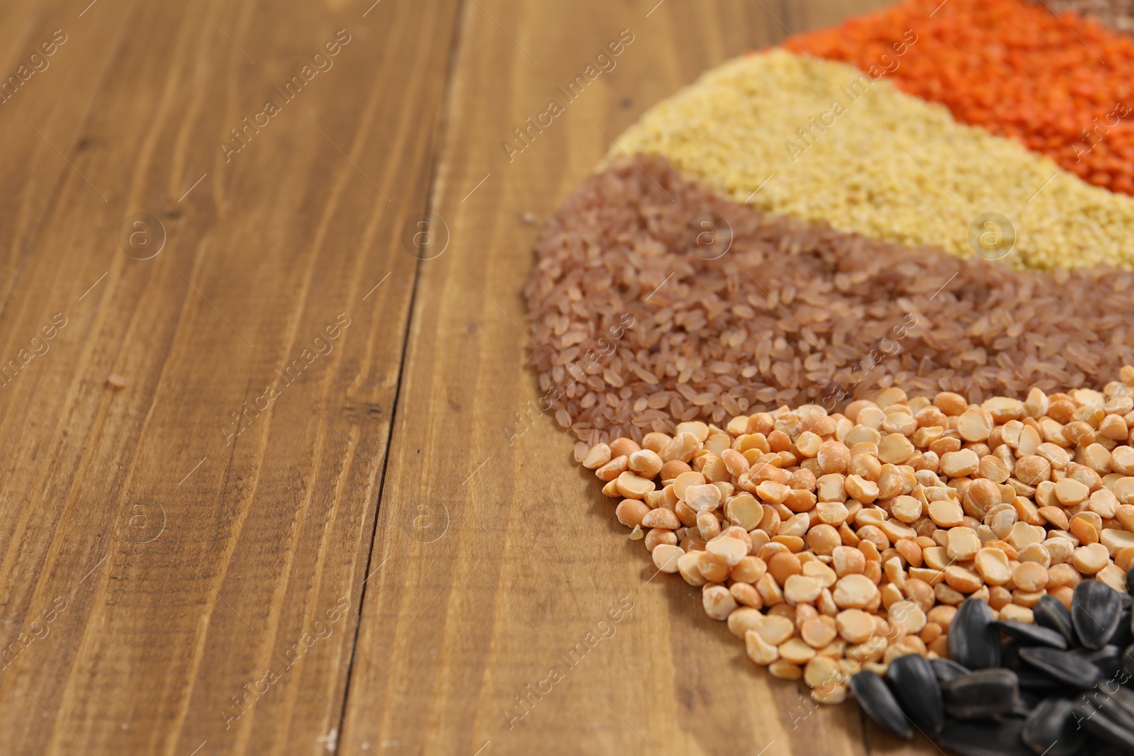 Photo of Different types of cereals, legumes and seeds on wooden table, closeup. Space for text