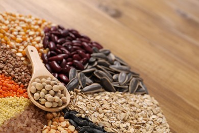 Photo of Different types of cereals, legumes and seeds with spoon on table, closeup