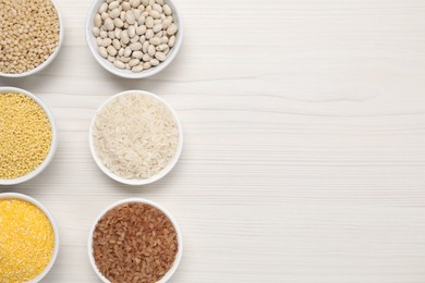 Photo of Different types of cereals and legumes in bowls on white wooden table, flat lay. Space for text